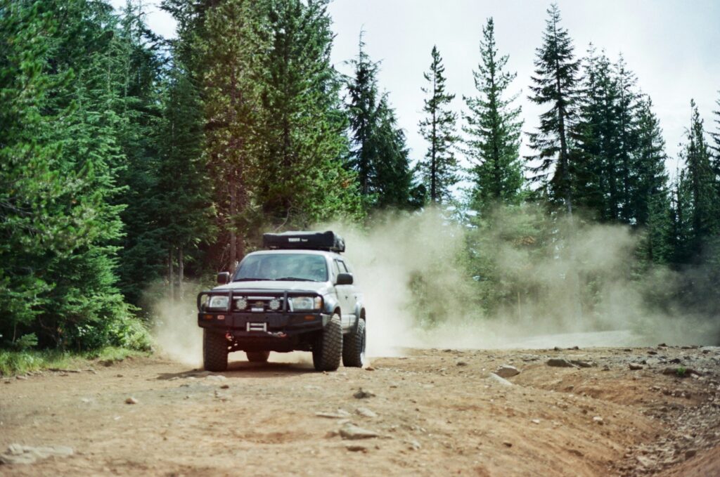 A rugged 4WD SUV kicking up dust while driving on a gravel forest service road in the remote wilderness of Prince of Wales Island, Alaska.