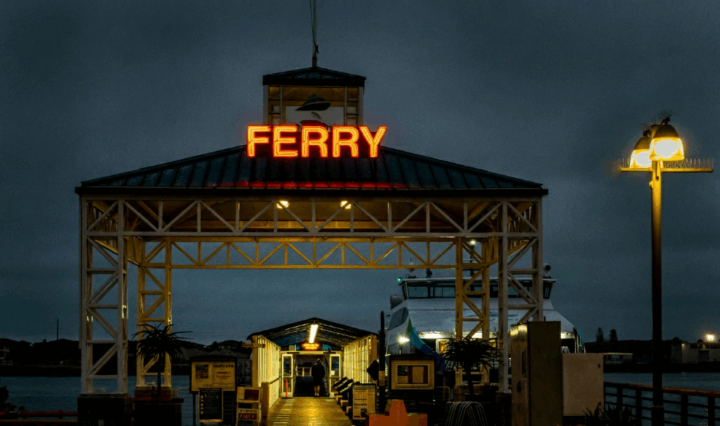 The entrance to the Ketchikan ferry terminal at night with a bright neon "FERRY" sign, the starting point for taking a rental car to Prince of Wales Island
